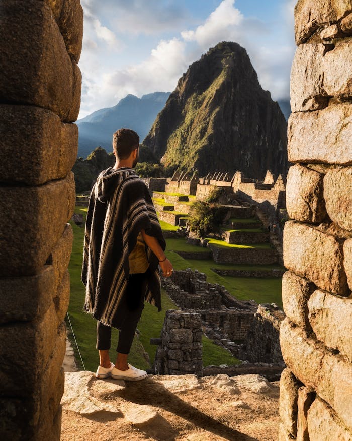 A man in traditional clothing overlooks the ancient ruins of Machu Picchu during daytime.