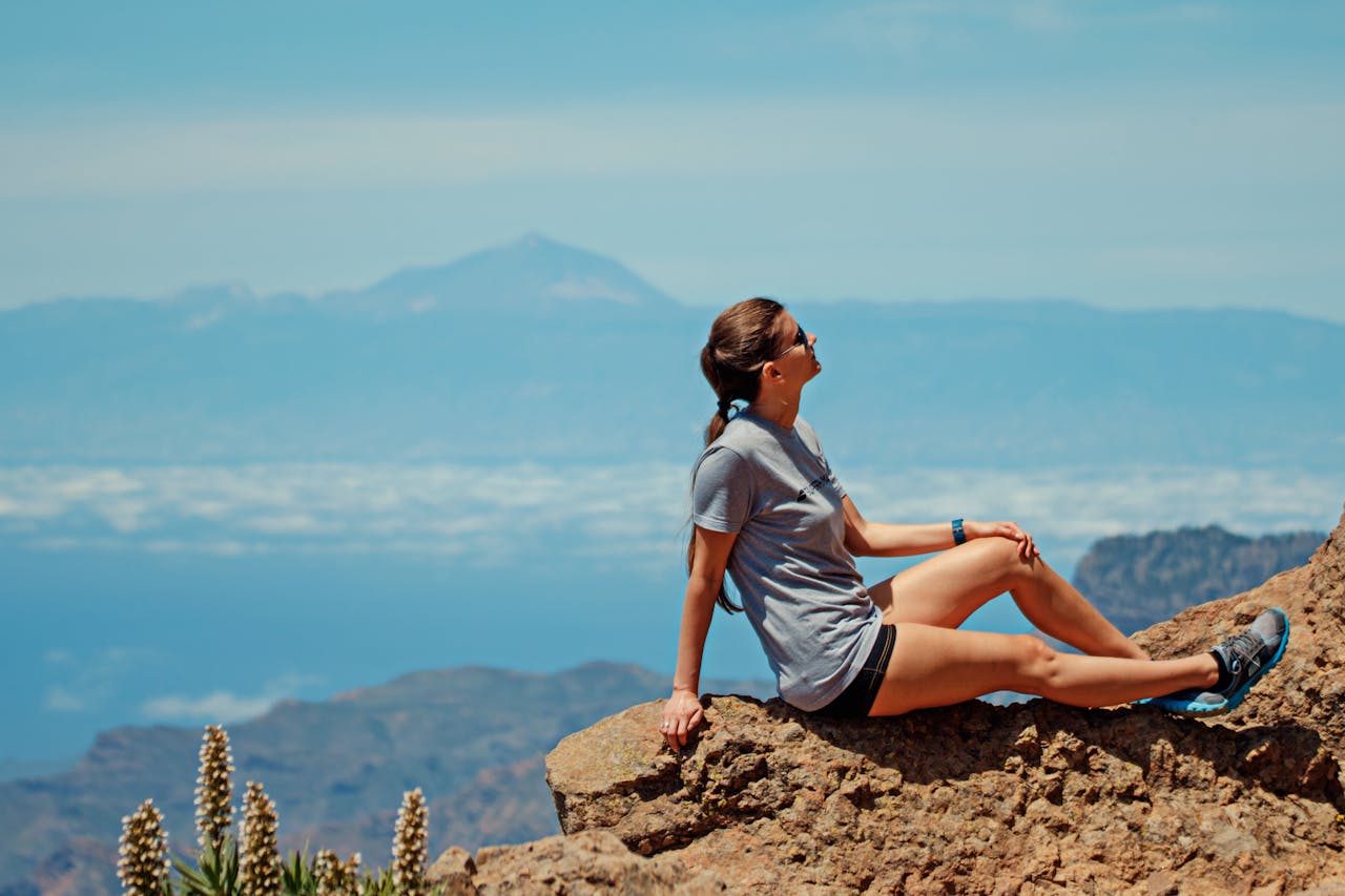 A woman relaxing on a rocky mountain with a scenic view under a blue sky.