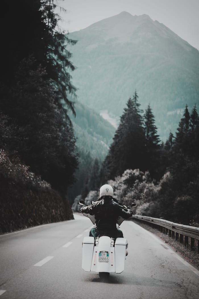 A solo motorcyclist enjoys a picturesque ride through a winding mountain road surrounded by lush forest.
