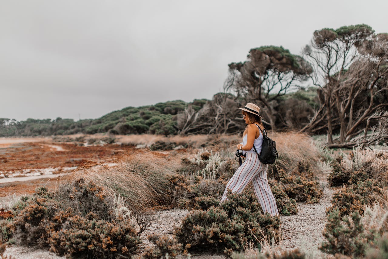 A woman with a backpack walks through a scenic coastal landscape with unique trees.
